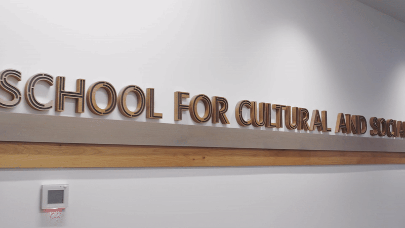 a gif that pans the wooden decorative text "School for Cultural and Social Transformation" feature outside the School offices in Gardner Commons