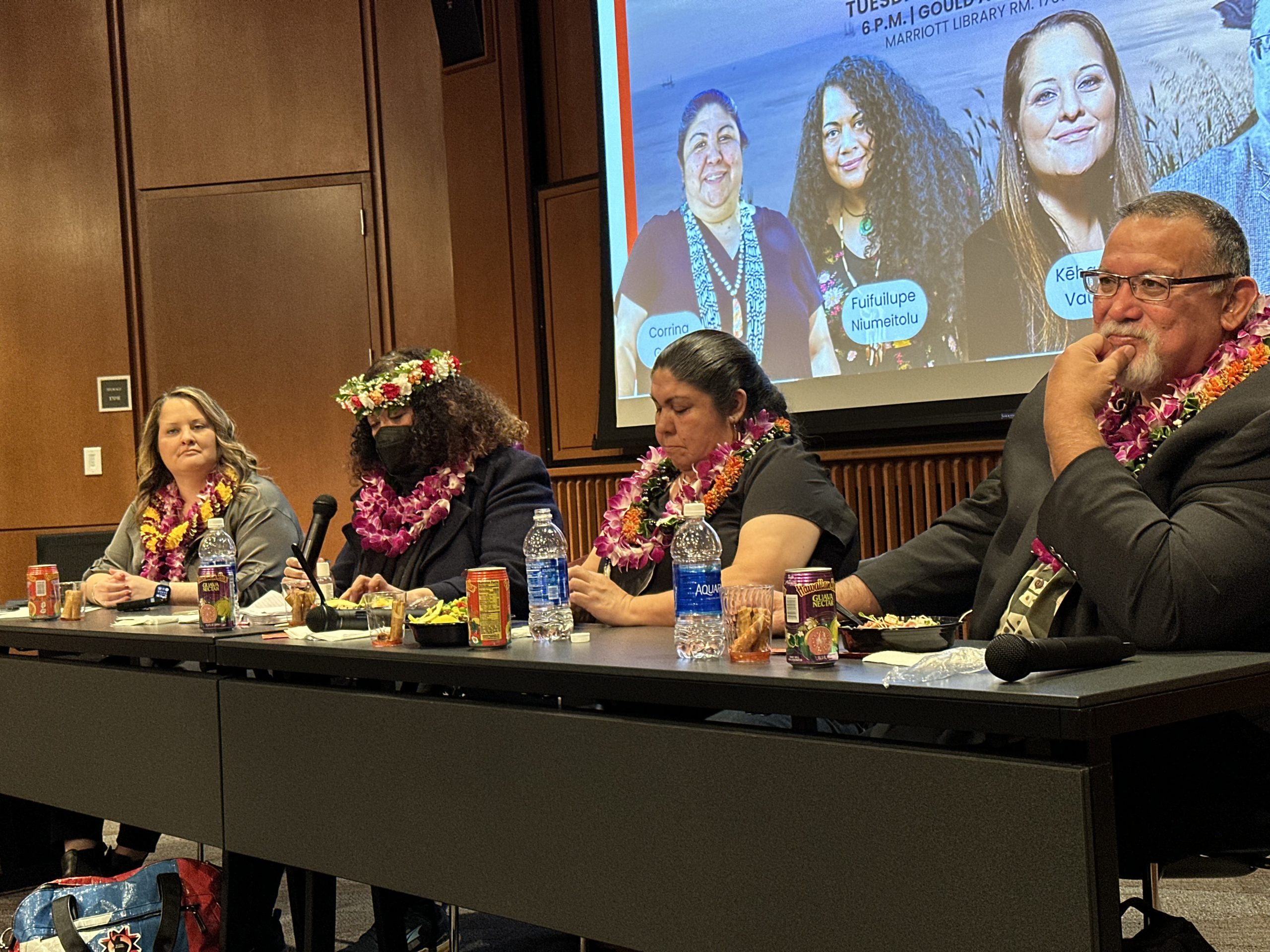 Four Pacific Islander elders sit at a panel table; they each have a lei around their neck